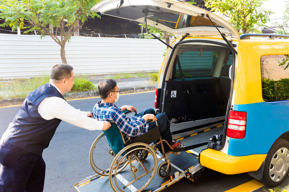 driver helping man on wheelchair getting into taxi